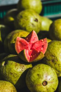 A pile of ripe green guavas with a vibrant pink sliced guava on top, highlighting freshness.
